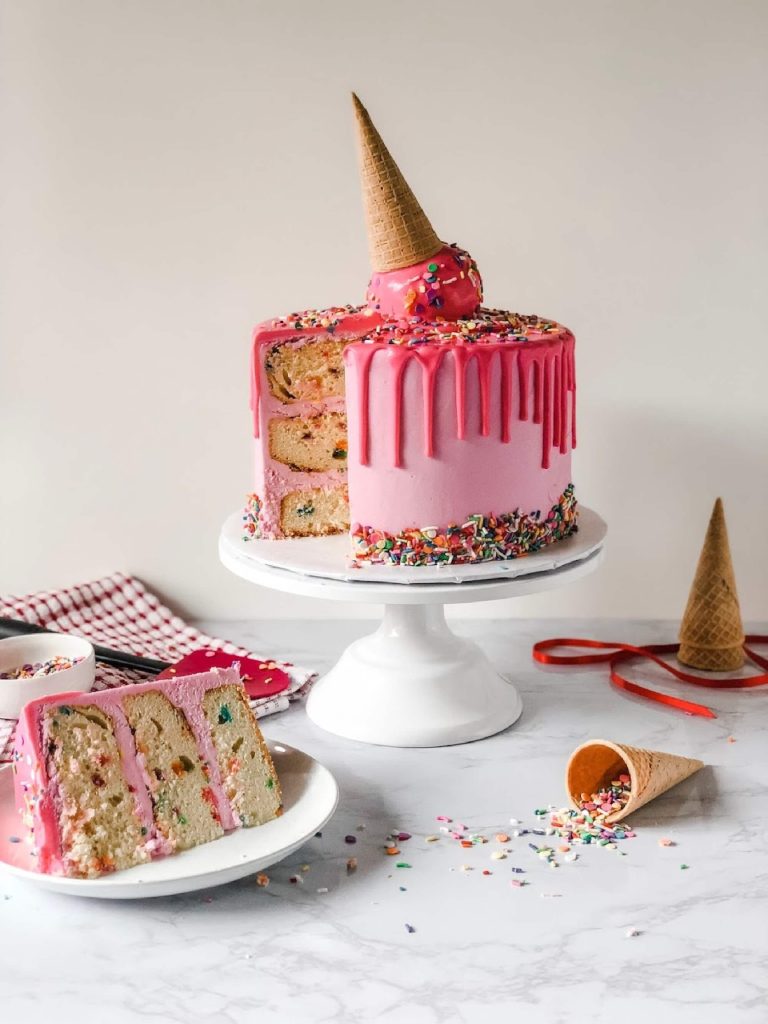 birthday cake with pretend ice cream cone on top made from cake with pink drizzle down the sides and sponge filling