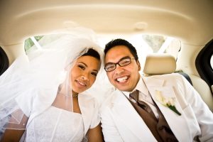 An asian couple smiling in a wedding car dressed in bride and groom traditional dress